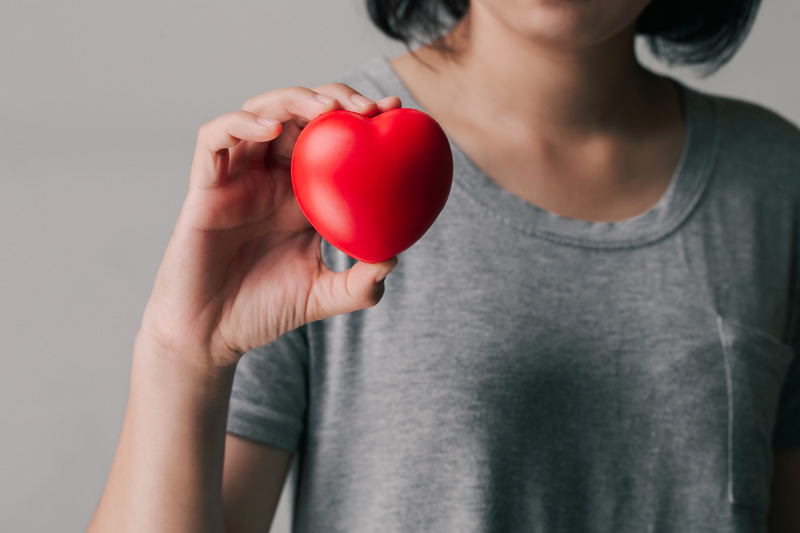 A women in a grey top holding a red heart.