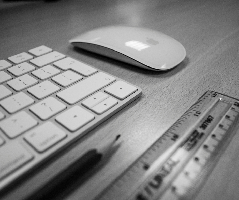 An apple mouse and keyboard on a desk with a ruler and pencil