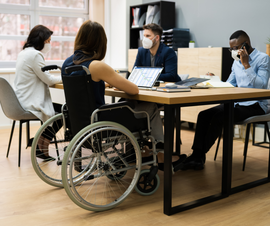 people sat at a desk working together, one person is sat in a wheelchair