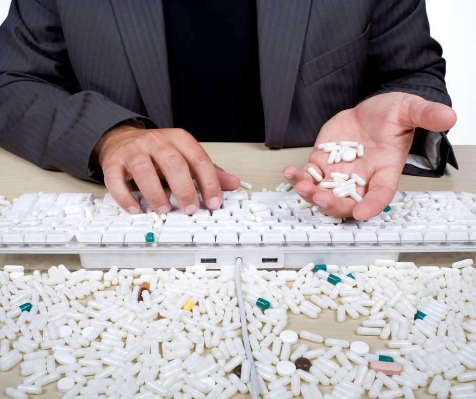 Man with one hand on a keyboard, the other holding many pills